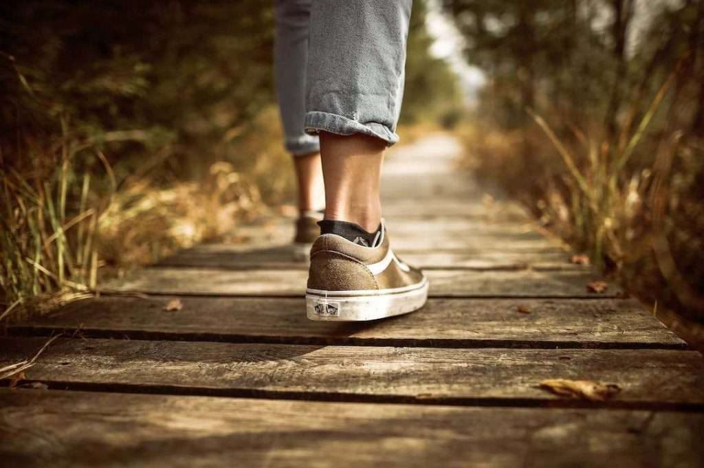 A photo of a person walking on a brown pathway wearing Vans sneakers