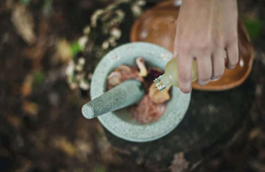 A photo of a person pouring liquid from bottle inside mortar and pestle