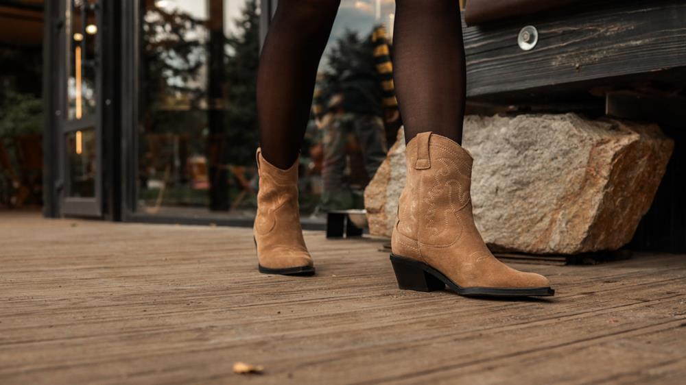 Woman's legs in black tights and stylish brown suede cowboy boots on wooden deck