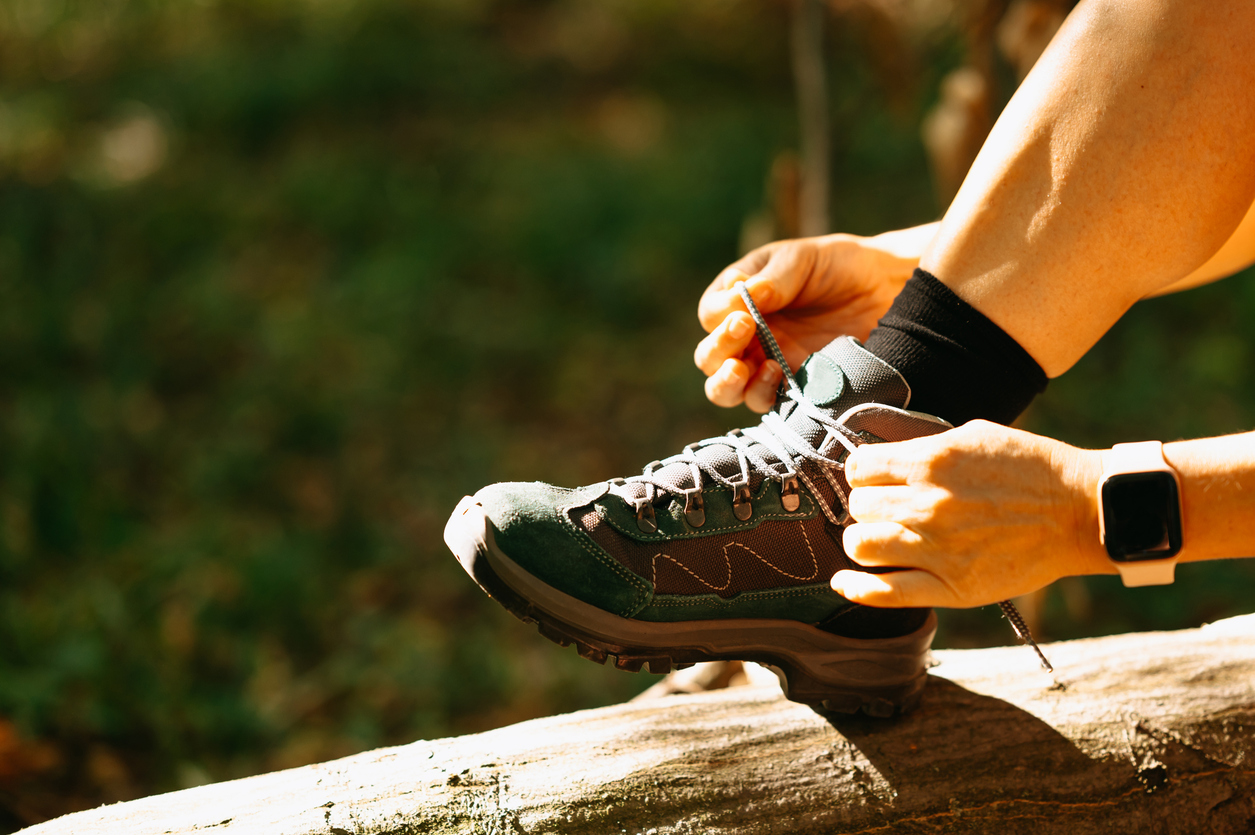 a person tying shoelaces on her hiking shoes in the forest